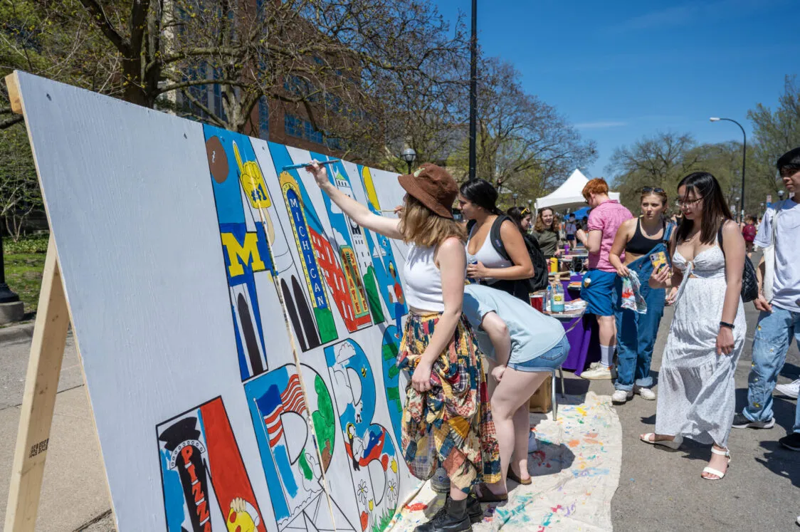 Three friends are painting a large sign that reads Ann Arbor.