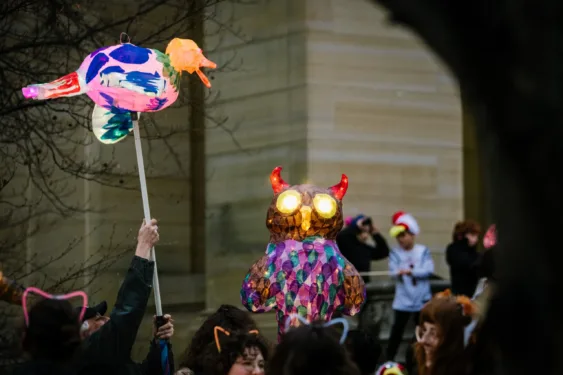 A group of people holding up lanterns on a dark evening. One lantern is an owl and one is a duck.