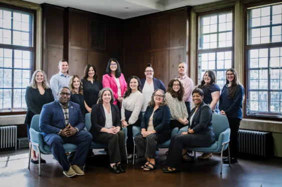 The Dean of Students staff seated in a room with dark stained wood paneling. Light filters in through windows behind them.