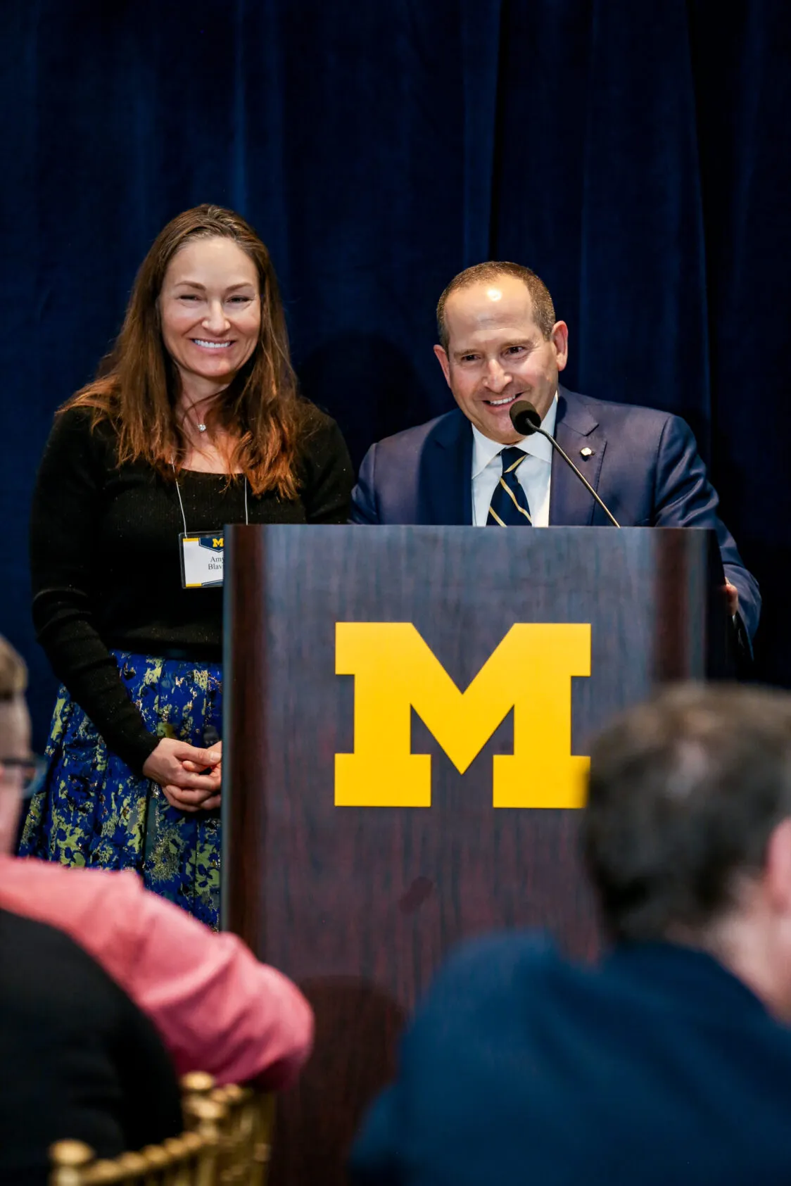 Paul and Amy Blavin speak at a lectern. Amy is on the left and Paul is on the right.