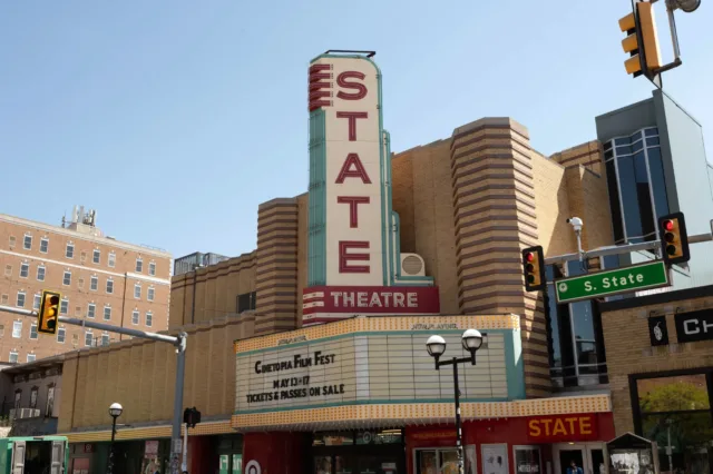 A low-angle shot of the historic State Theatre building on a clear day, highlighting its tall, vertical retro sign and a marquee advertising the Cinetopia Film Fest.