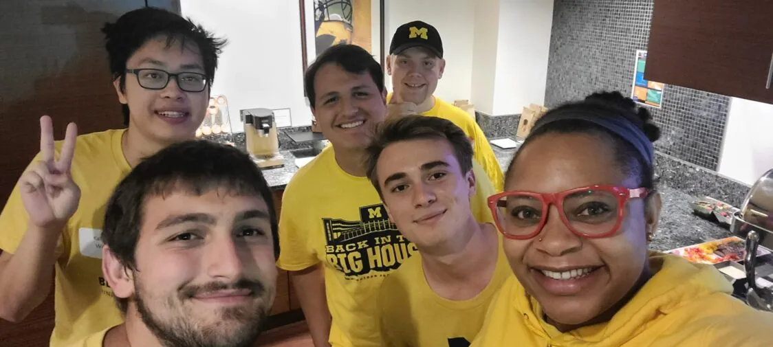 Six students, all wearing yellow shirts, smile for a selfie.