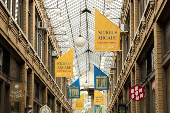 A view of the Nickels Arcade glass ceiling and brickwork. Blue and yellow flags line the arcade in celebration of the Arcade’s centennial in 2017.