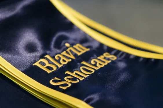 Close-up of folded blue graduation stoles with maize trim, featuring embroidered maize text that reads Blavin Scholars.