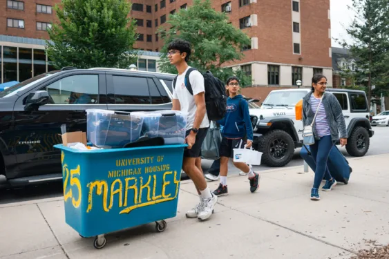 A new student and their family pushing a cart full of belongings during campus move-in.
