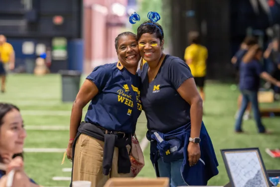 Two people dressed in Michigan gear smile for a photo a the Parent and Family Weekend Tailgate.