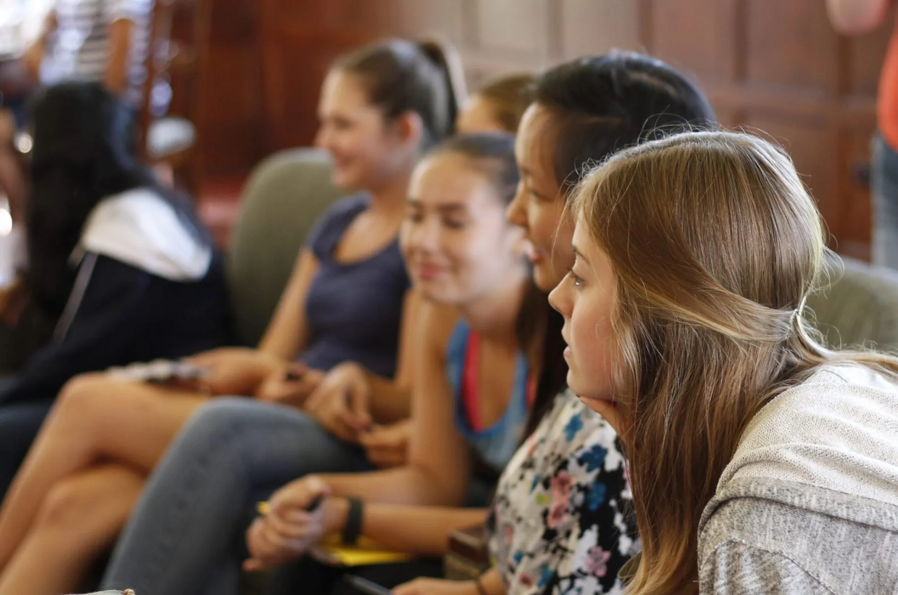 A group of students are listening to someone off to the left of the photo. The woman closest to the viewer has an engaged, interested look on her face.