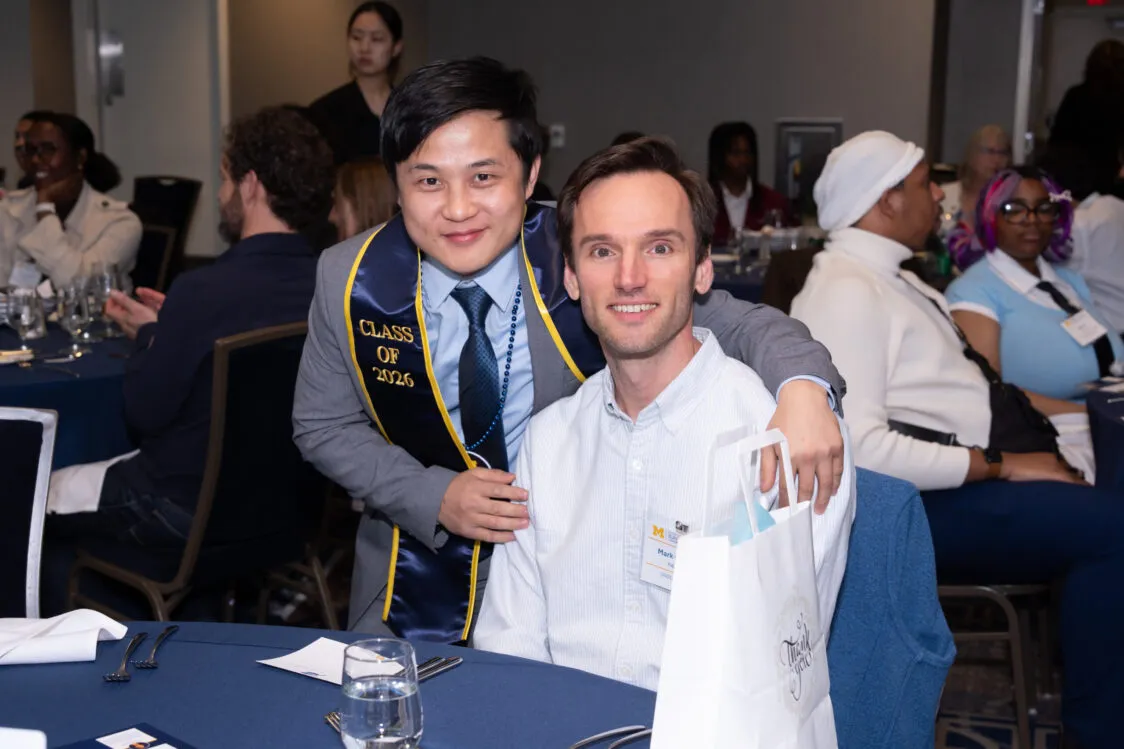 A Blavin Scholar wearing a suit and a Blavin Scholars stole, poses with his mentor, a man in a blue button up shirt.