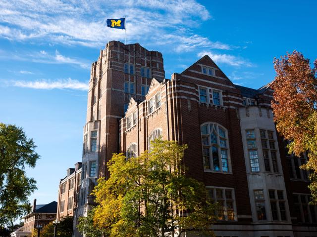 The Michigan Union with a block M flag flying atop in front of a blue sky