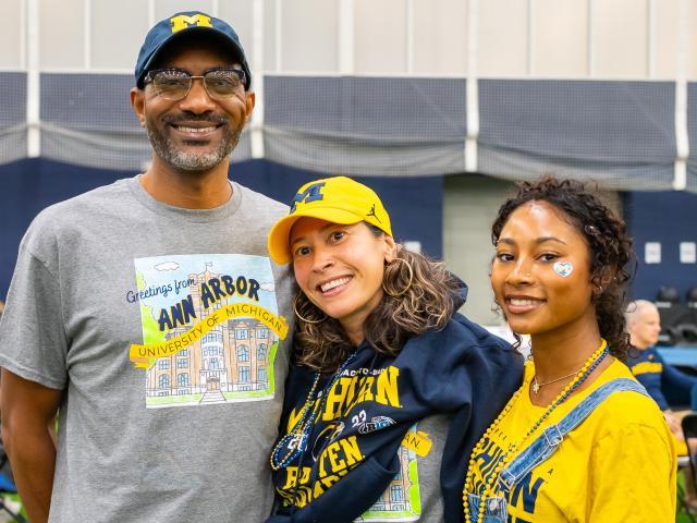 Three people dressed in U-M gear pose for a picture at Oosterbaan Fieldhouse during PFW 2025